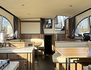 Avalon Salon, Blickrichtung nach achtern, vorne links Teile der Pantry, rechts Sitzbank mit Tisch, dahinter die Sitzbank steuerbords, Backbord der Aufgang zum Achterdeck