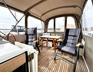 Linssen GS 35 Mi Tiempo Achterdeck, Blick auf Sitzgruppe am Heck, davor Tisch und Klappstuhl. Links Steuerstand mit Holzsteuerrad und Chromspeichen, davor Fahrersitz