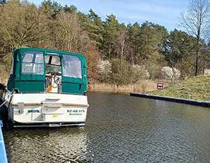 Linssen 29.9 Wedis mit grünem Verdeck am Anleger mit Stromanschluss. Blick von Heck an die Backbordseite nach vorne. Rechts anderes Ufer.