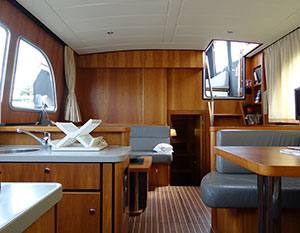 Linssen 29.9 Wedis Innenansicht. Blick nach achtern, rechts hinten der Aufgang mit offener Luke, links vorne Spüle rechts Teil der grauen Sitzbank und Tisch