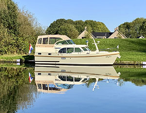 Linssen GS 35 AC am Ufer, grüner Rasen dann Deich, im Hintergrund Giebel von Häusern. Blick auf Steuerbordseite, Verdeck geschlossen, blauer Himmel ©Linssen Yachts